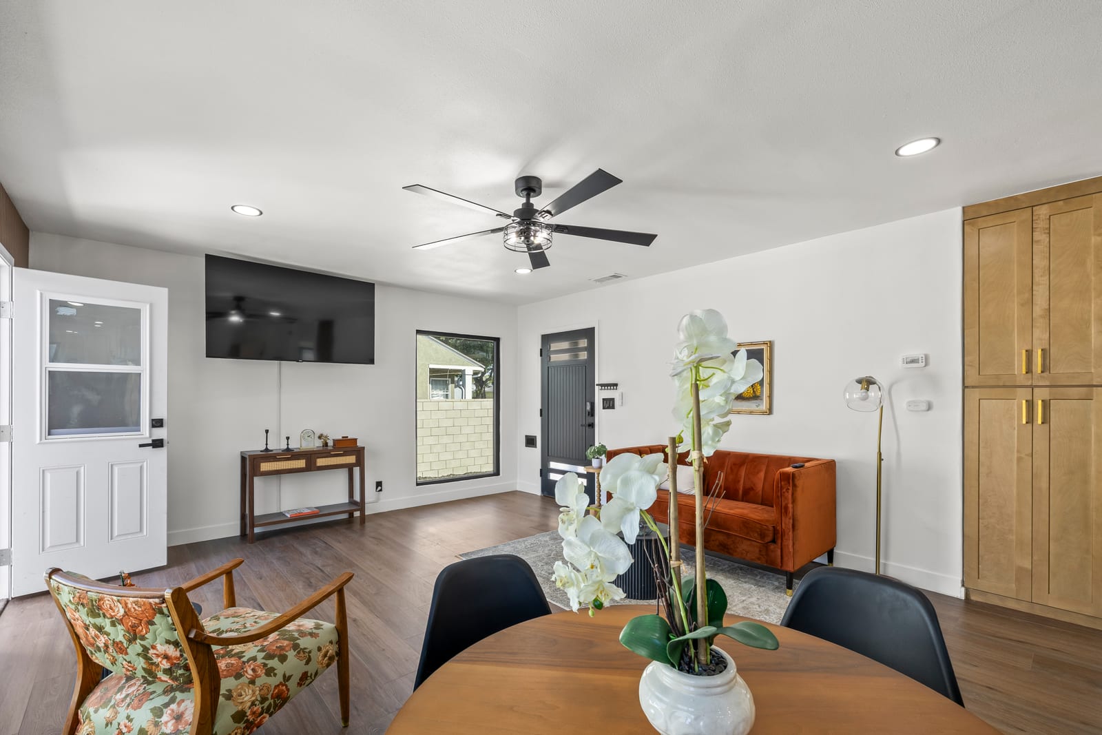 Open living and dining room with a round table, a ceiling fan and tall wood cabinets