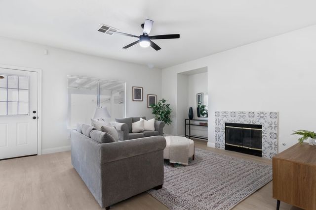 Living room with gray sofas, a ceiling fan and a fireplace framed in patterned tile