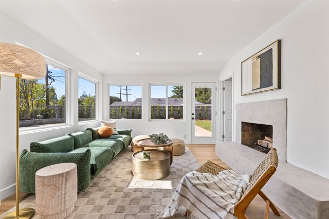 Sunlit living room in a Claremont home with a plaster fireplace, a green sofa, a row of windows and a door to the back lawn