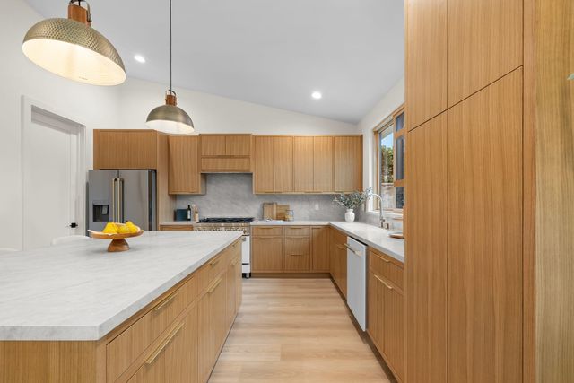 Kitchen with a long stone island, wood cabinetry and a range under a vaulted ceiling