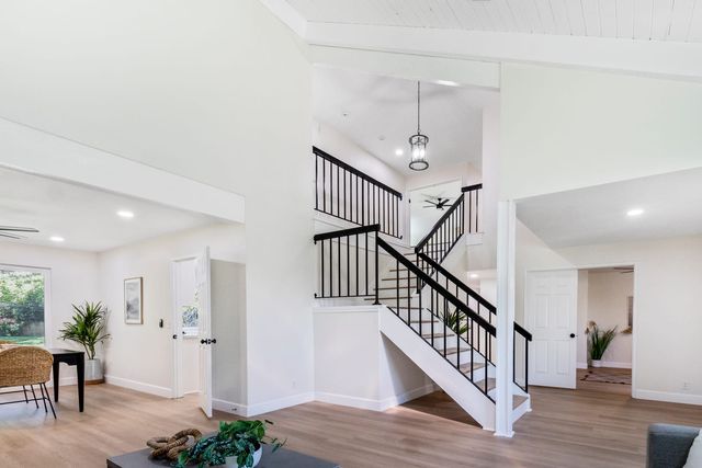 A split-level interior with a vaulted plank ceiling and a white staircase with black iron balusters rising between two rooms