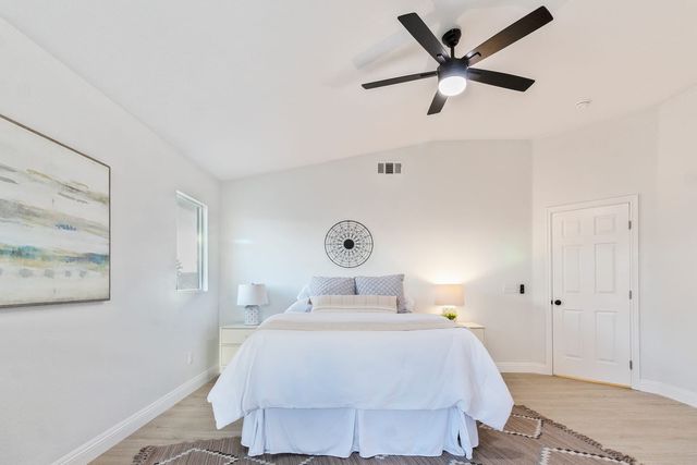 A bedroom with a vaulted ceiling, a black five-blade ceiling fan, a made bed between two lamps, and a six-panel door