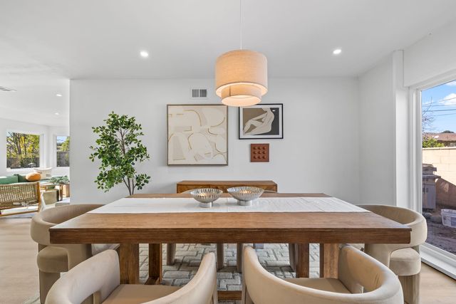 A wood dining table with cream upholstered chairs under a linen drum pendant in a bright Claremont dining room, with a glass door to the side yard