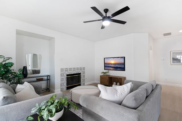 Staged living room with gray sofas, a patterned tile fireplace surround, a wall-mounted television and a black ceiling fan