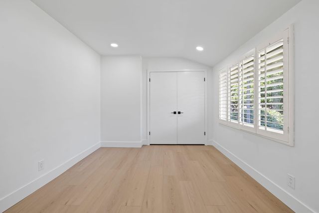 Empty room with light wood floors, recessed lights, white double closet doors and plantation shutters on a wide window