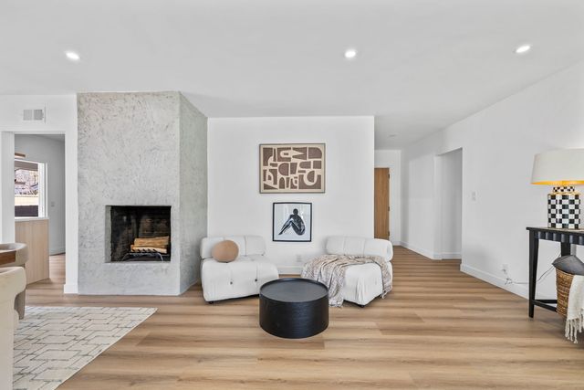 Living room with a textured plaster fireplace, two white lounge chairs, a round black table and wood plank floors
