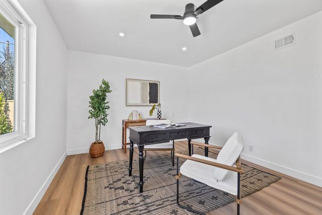 Staged home office with a dark wood writing desk, a white upholstered chair and a potted plant beside a window