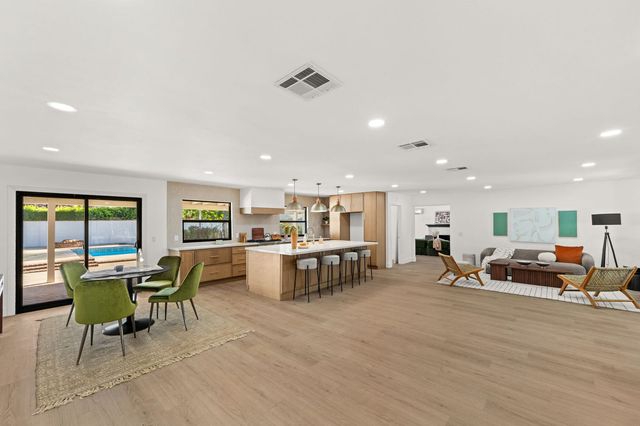 Open great room with a dining table, a kitchen island and glass doors to a pool