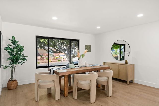 Staged dining room with a long wood table, four upholstered chairs and a picture window looking onto a tree-lined residential street