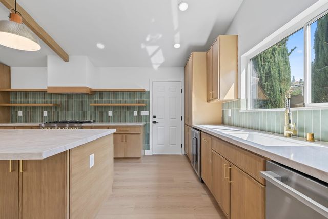 Kitchen in a Claremont home with oak cabinets, a green tile backsplash and a window over the sink looking out to tall cypress trees and a hillside