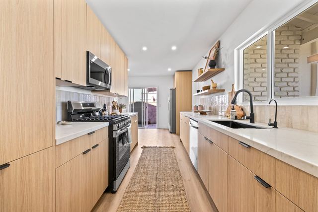Galley kitchen in a Claremont home with light oak cabinets, a jute runner and a sliding glass door at the far end opening to the back patio