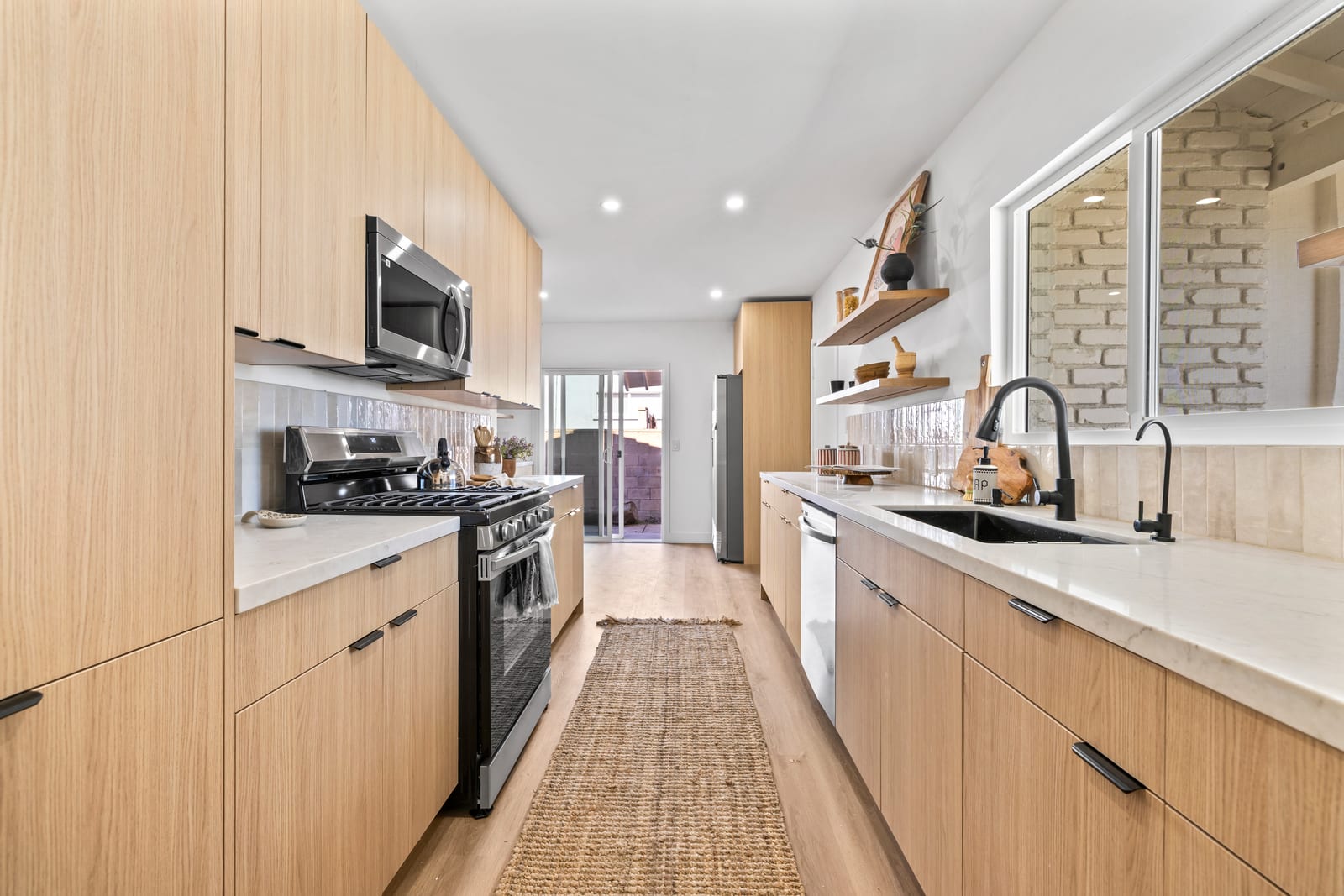 Galley kitchen in a Claremont home with light oak cabinets, a jute runner and a sliding glass door at the far end opening to the back patio