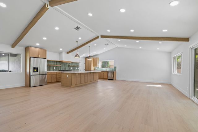 Empty great room in a Claremont house with exposed wood beams on a vaulted ceiling, an oak kitchen island and light plank floors