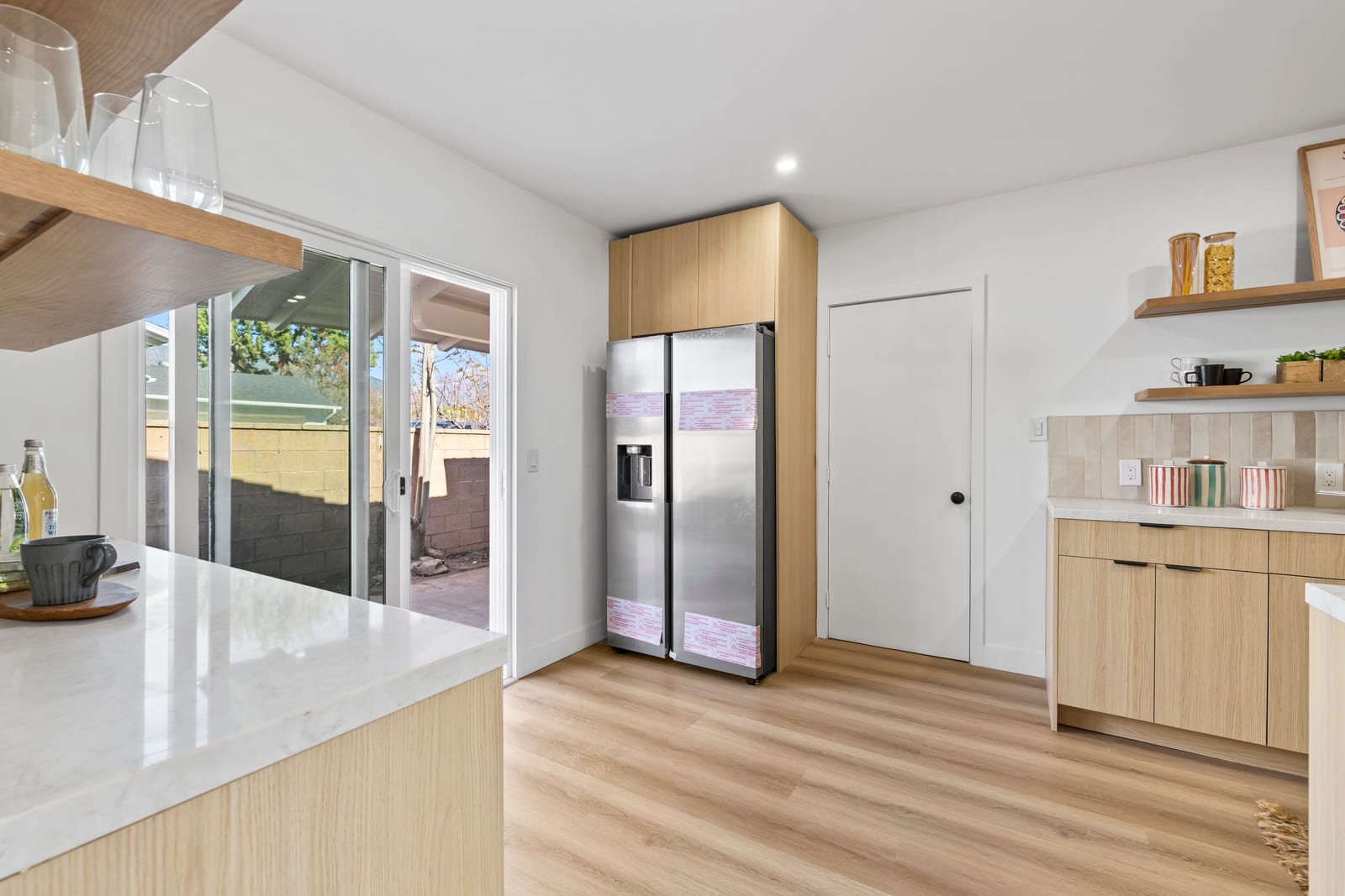 Renovated kitchen in a Claremont house with light oak cabinets, a stainless refrigerator still in its protective wrap and a sliding glass door to a walled patio