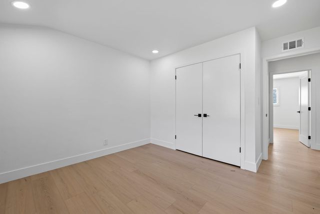 Empty bedroom in a Claremont house with white walls, wood-look flooring, a double-door closet and an open doorway to the hall