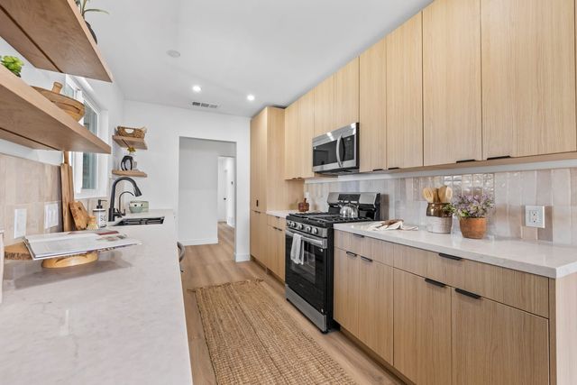 Galley kitchen in a Claremont home with light oak cabinets, white stone counters, a gas range and open wood shelving