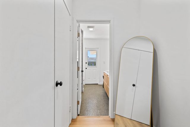 A white hallway in a Claremont house with a gold-framed arched floor mirror, looking through a doorway into a bathroom with penny tile flooring, a wood vanity and a half-glass back door