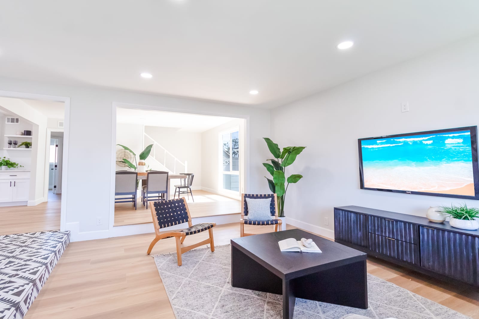Living room with a long low media console, two woven chairs and a view through to the dining area