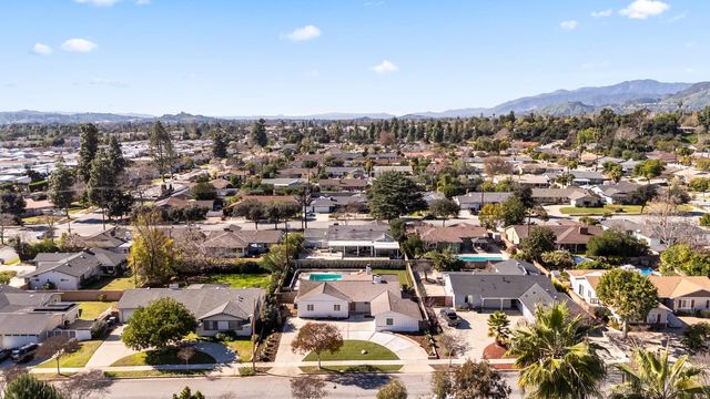 Aerial view over a Claremont neighborhood of single-story ranch homes with backyard pools and mature trees, looking toward the San Gabriel Mountains