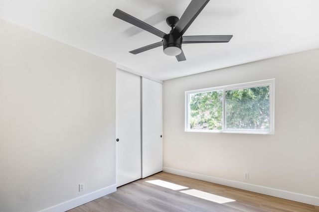 Empty bedroom with a ceiling fan, sliding closet doors, wood-look flooring and a window onto green trees