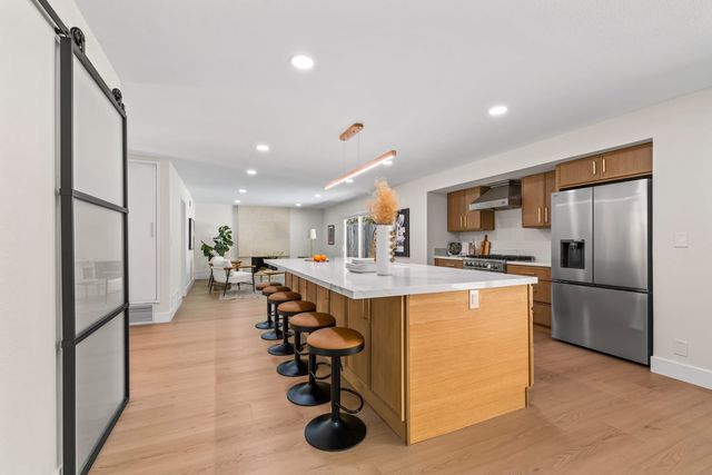 Remodeled kitchen with a long wood island, five bar stools and stainless appliances, with an open living area beyond