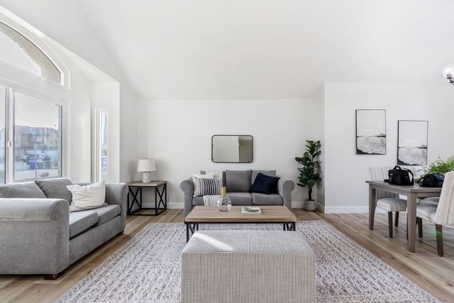 Vaulted living room with two sofas, an ottoman and a dining table by the window