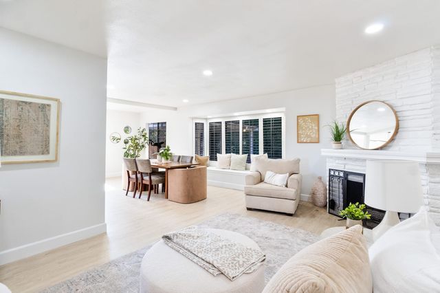 Living room with a white brick fireplace, plantation shutters and a dining table beyond