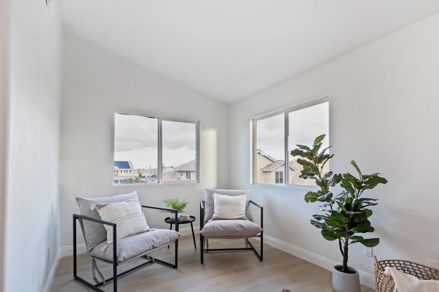 A small staged room with two armchairs and a potted plant, its windows looking out over neighboring two-story tract houses with tile roofs.