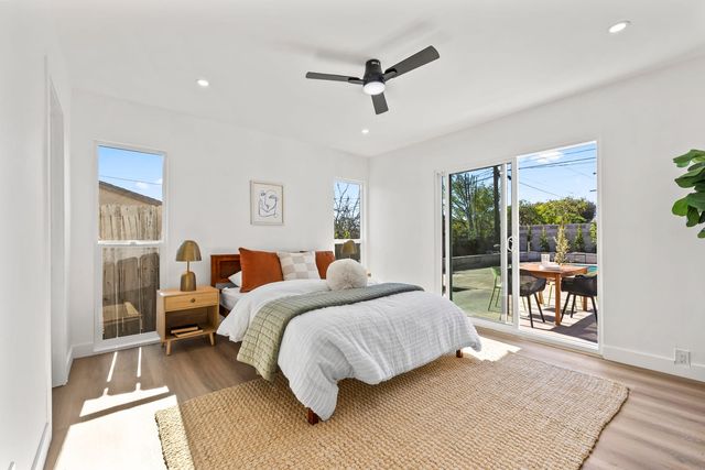 Bright bedroom with a made bed, a wood nightstand and a ceiling fan, sliding glass doors opening to a patio with a dining table