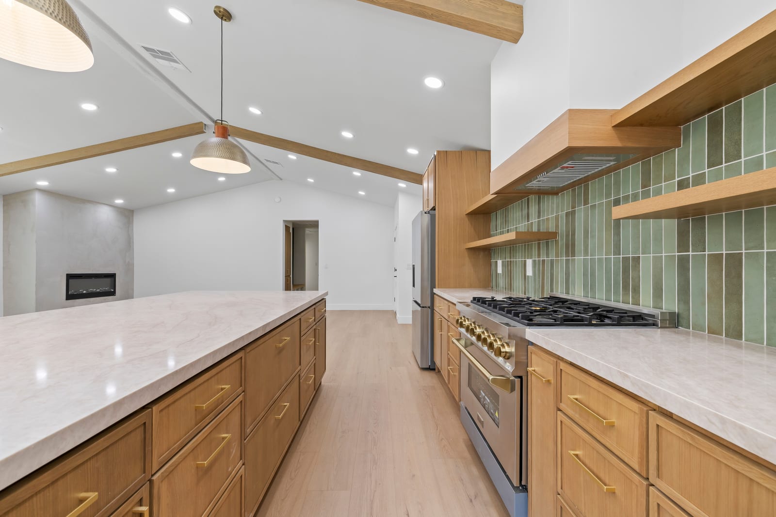 Remodeled kitchen with a long stone-topped island, oak cabinets, a gas range and green tile backsplash under a beamed vaulted ceiling